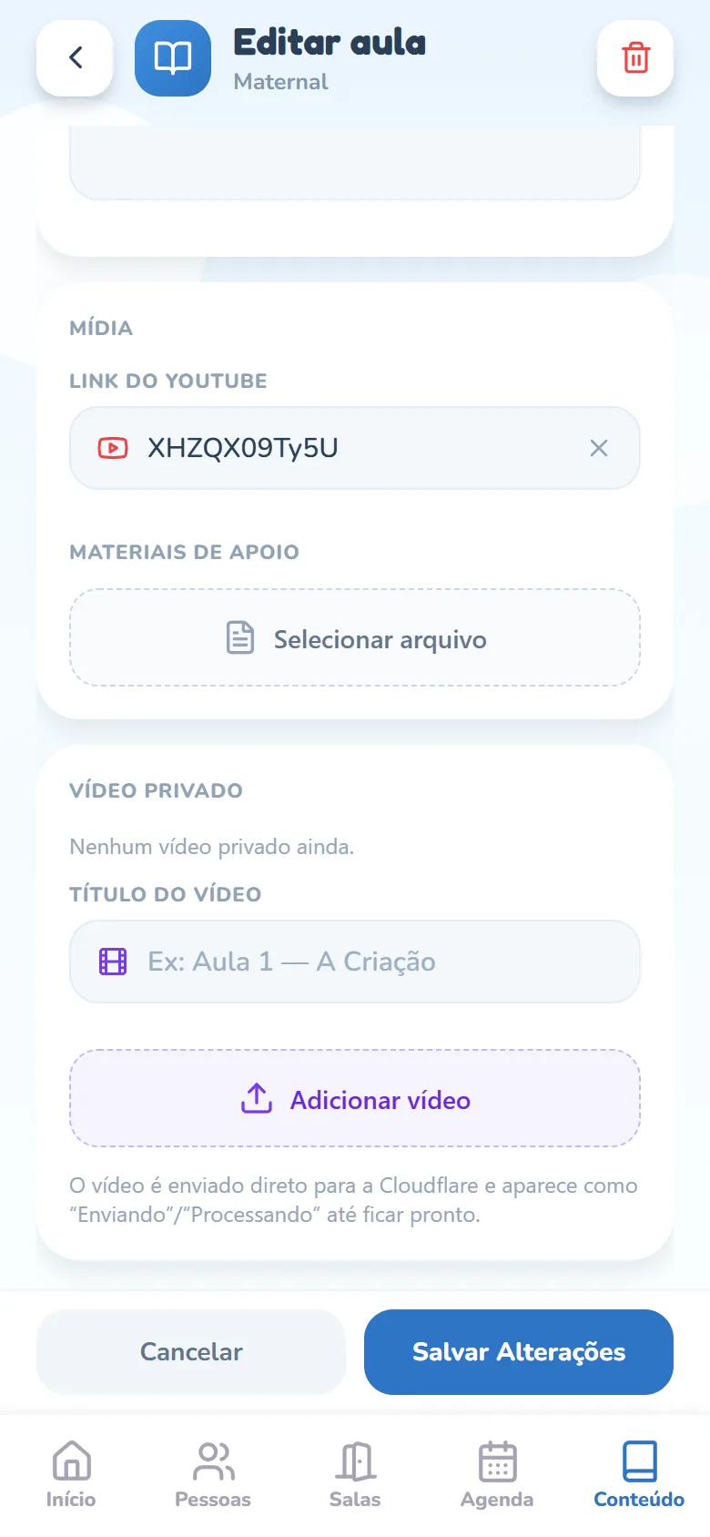 Tela Editar aula rolada até o cartão Mídia: o campo Link do YouTube com o vídeo já salvo (o ícone vermelho do YouTube e o código do vídeo) e um X para limpar, o rótulo Materiais de Apoio e o botão tracejado Selecionar arquivo; embaixo, o cartão Vídeo privado com Nenhum vídeo privado ainda, o campo Título do vídeo, o botão Adicionar vídeo e a nota de que o envio vai direto para a Cloudflare; no rodapé, Cancelar e Salvar Alterações.